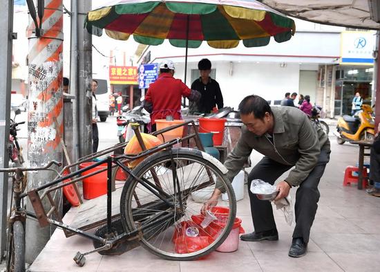 一名賣卷筒粉的攤主在廣西橫縣橫州鎮(zhèn)街頭將不同的垃圾分類投放到4個(gè)垃圾袋里(4月13日攝)。 新華社記者 周華 攝